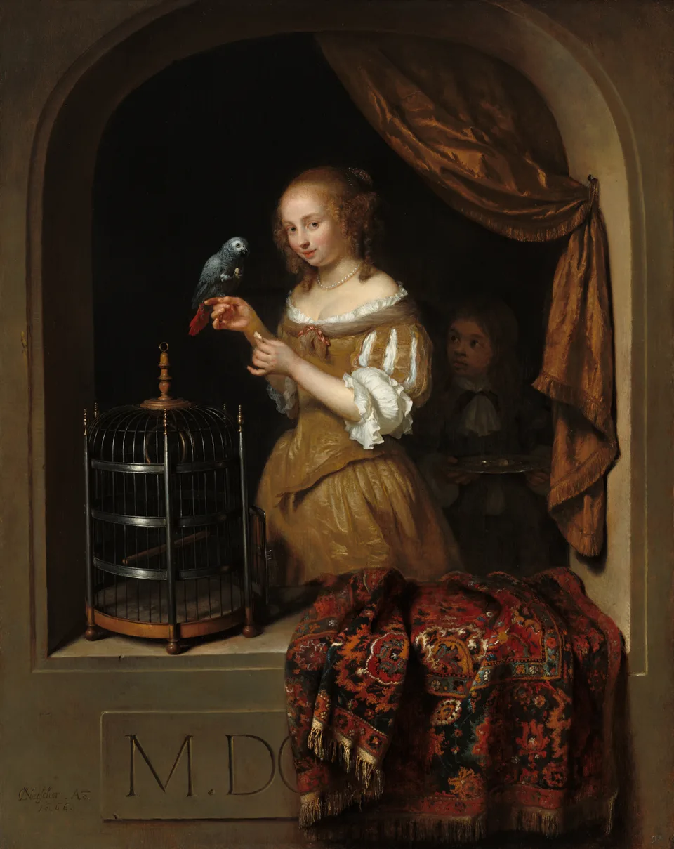 A young woman in a golden-brown gown feeds a grey parrot held on her finger, with an open cage beside her and a page boy holding a silver tray in the shadow behind.